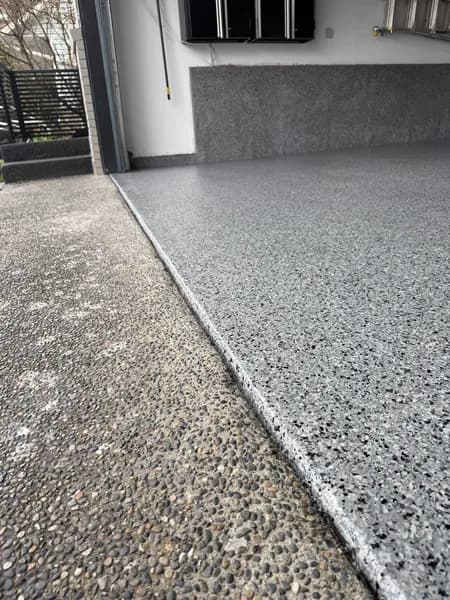 Close-up of a grey flake epoxy garage edge meeting an aggregate concrete driveway