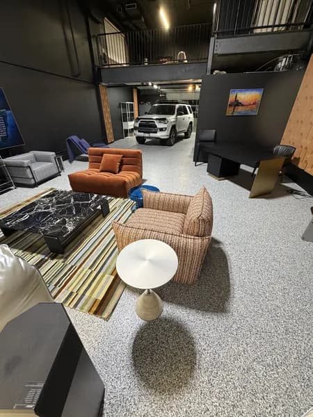 Grey flake epoxy floor in a studio showroom with lounge seating and a vehicle