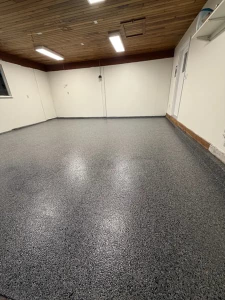 Dark grey flake epoxy floor in a finished basement with a wood-plank ceiling