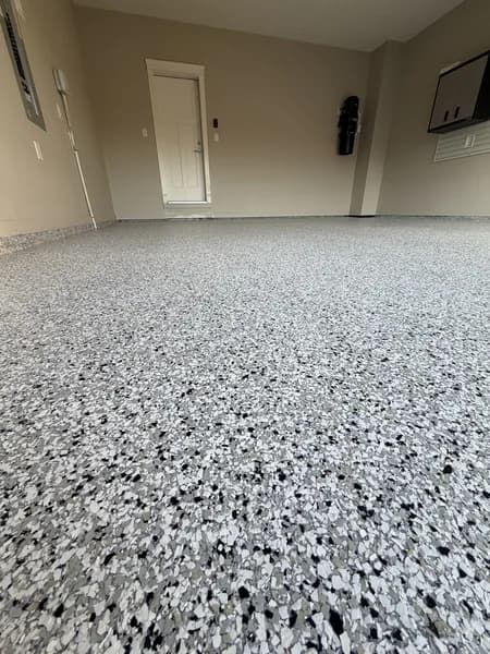 Grey, black and white flake epoxy garage floor viewed from a low angle near the entry door