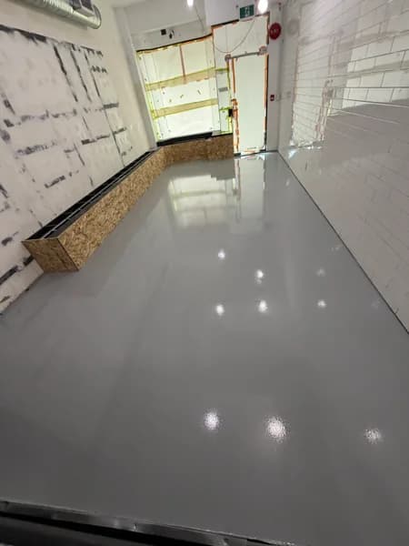Grey solid epoxy floor running the length of a white-tiled commercial space in Vancouver, BC